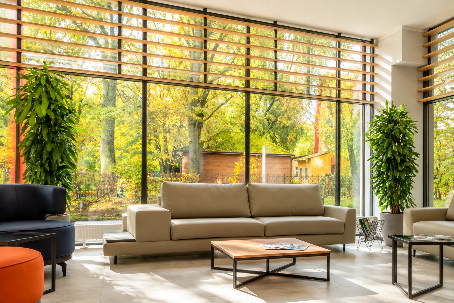 Bright all-season room with a beige sofa, tall windows, and views of golden autumn trees.