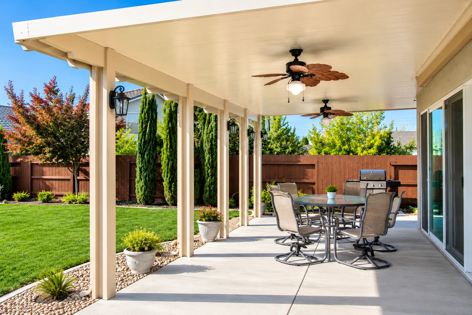 Covered patio with a cream-colored roof, ceiling fans, and outdoor dining furniture beside a green lawn.