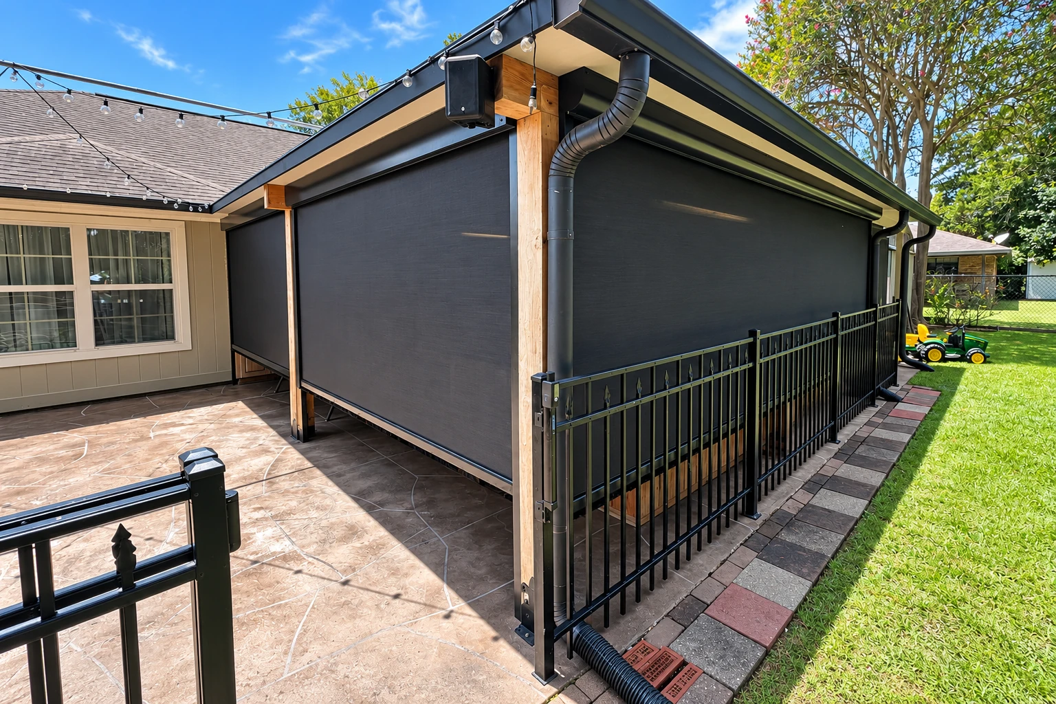 Screen room with dark mesh panels, wood posts and black railings beside a paved patio.