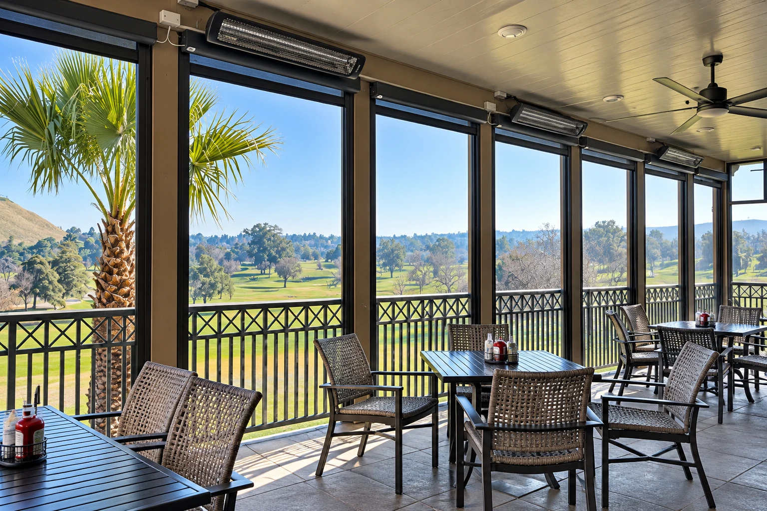 Sunroom addition with dark-framed windows, patio dining tables and chairs, overlooking a green golf course.