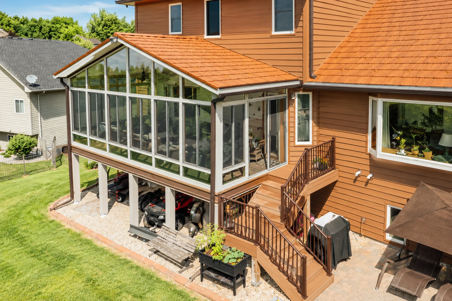 Raised sunroom addition with a terracotta gable roof and tall white-framed windows attached to a brown house.