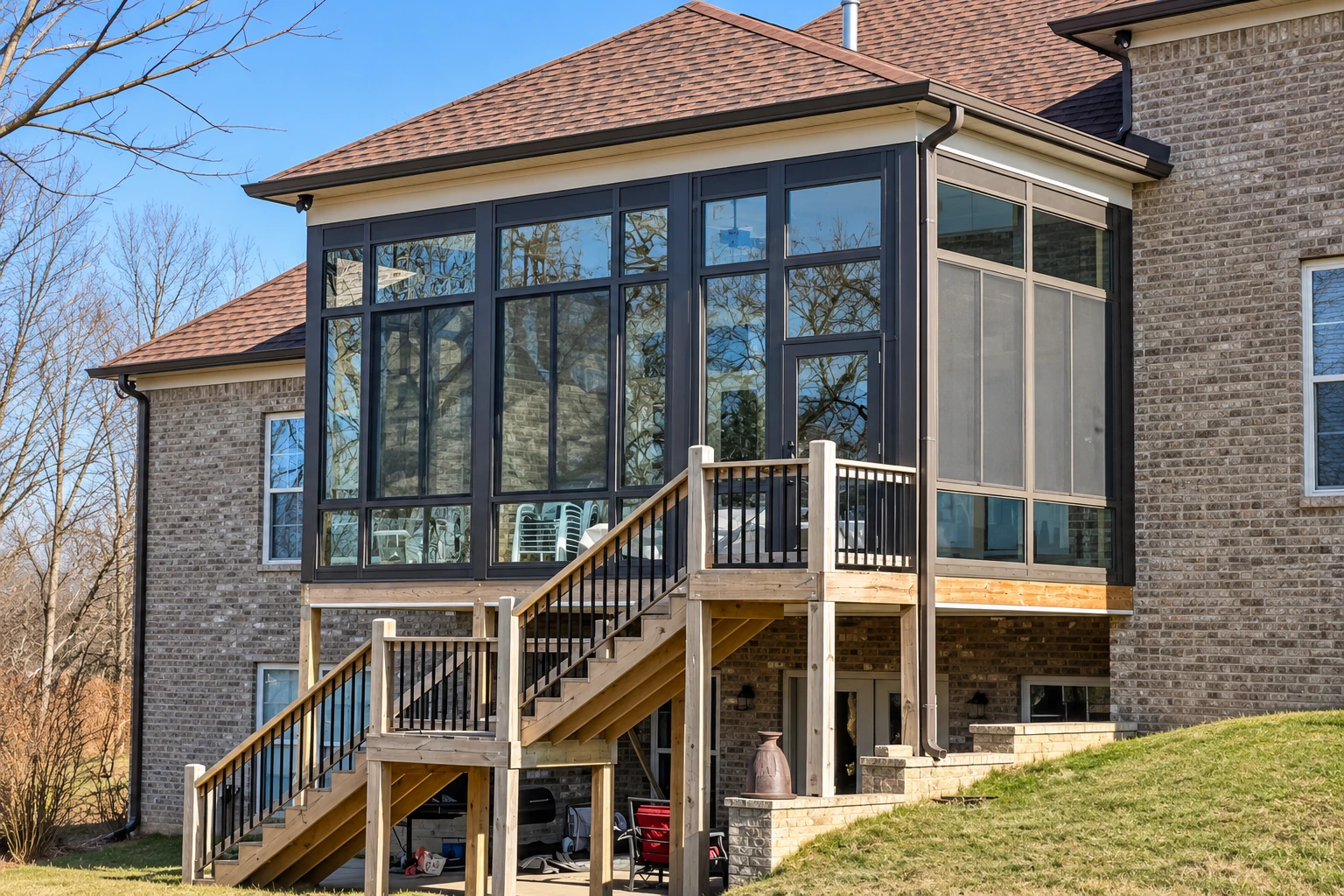 Dark-framed sunroom addition on a brick house, with a broad window wall and wooden stairs and deck.