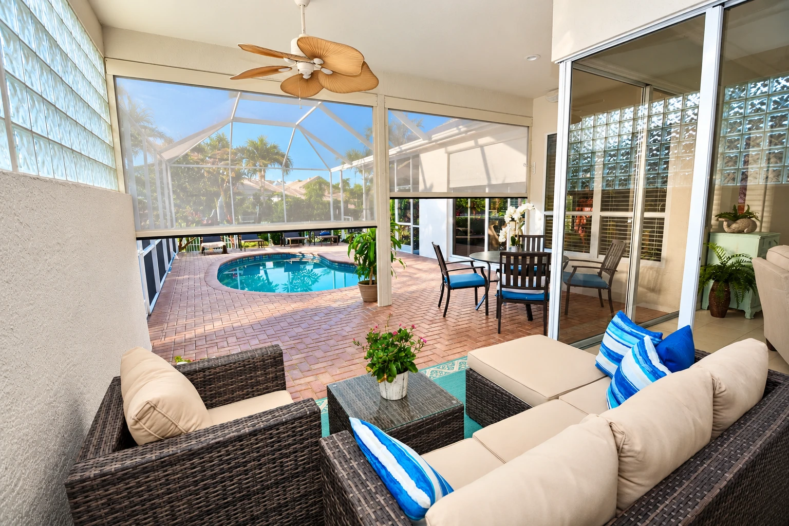 A remodeled sunroom opens onto a screened pool patio, with wicker seating, blue cushions, and a ceiling fan.