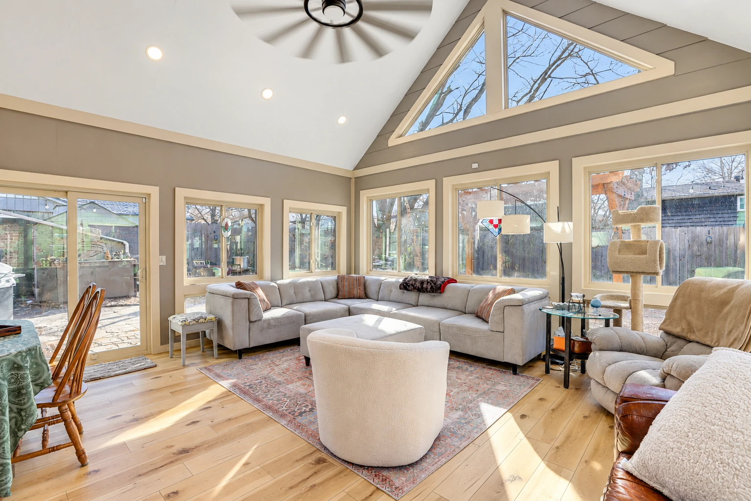 Bright sunroom living area with a vaulted ceiling, large windows, and a gray sectional arranged around a rug.